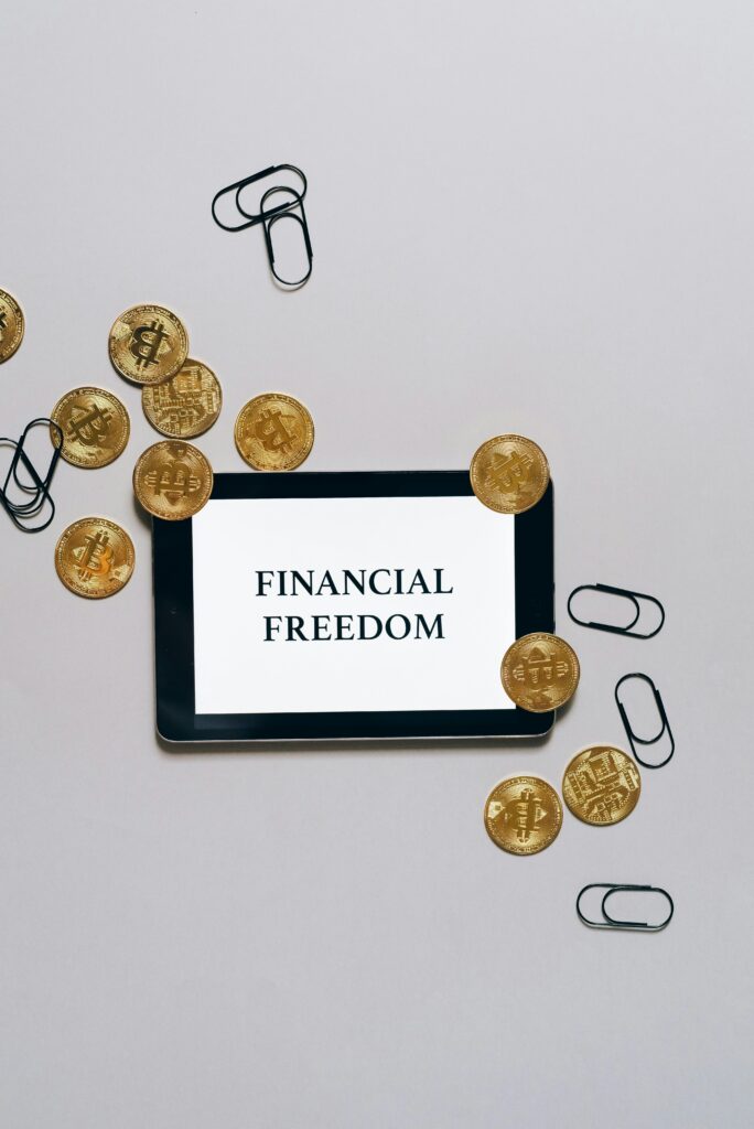 Top view of bitcoin coins and paper clips around a digital tablet displaying 'Financial Freedom'.